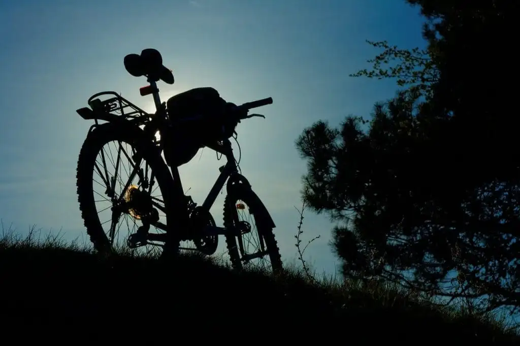Silhouette of a bicycle on a grassy hill with trees nearby, photographed against a bright sky near sunset—capturing one of the scenic things to do in Sunshine Valley.