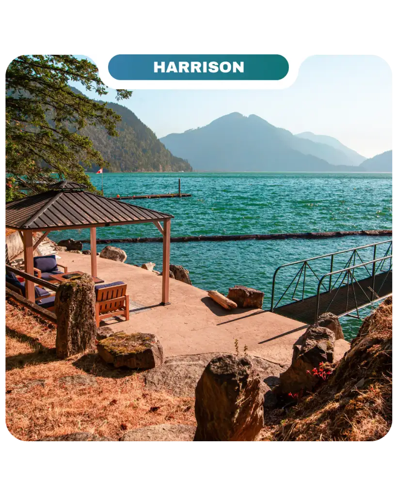 A lakeside patio with a gazebo, benches, and dock overlooks turquoise water and distant mountains under a clear sky at Harrison—perfect for relaxing and enjoying the Lifty Life.