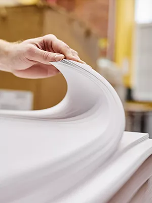 A person's hand flipping through a large stack of papers.