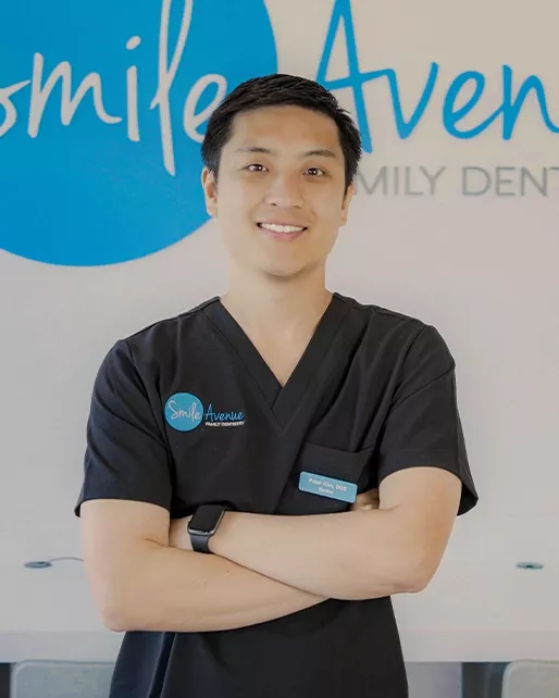 Male dentist in black scrubs with arms crossed, standing in front of Smile Avenue Family Dentistry sign in Katy, TX, highlighting family, emergency, and cosmetic dental care services.