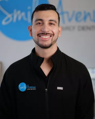 Smiling dentist at Smile Avenue Family Dentistry in black uniform with logo, providing family and emergency dental care in Cypress and Katy.