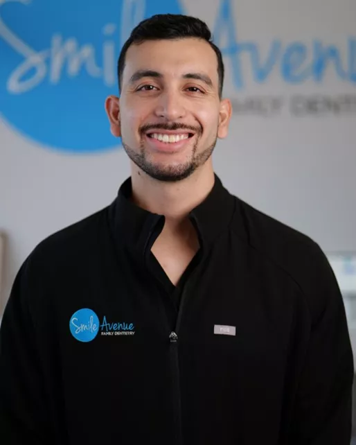 Smiling dentist at Smile Avenue Family Dentistry in black uniform with logo, providing family and emergency dental care in Cypress and Katy.
