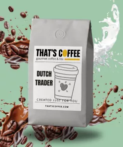 A gray bag of THAT'S COFFEE Dutch Trader blend is shown with a coffee cup illustration on the label, surrounded by splashes of coffee, milk, and coffee beans, highlighting premium coffee blends against a green background.