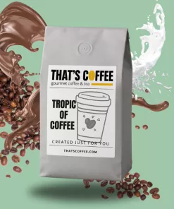 A gray bag of “That’s Coffee” labeled “Tropic of Coffee” sits upright, surrounded by swirling coffee blends, milk splashes, and scattered coffee beans on a green background.
