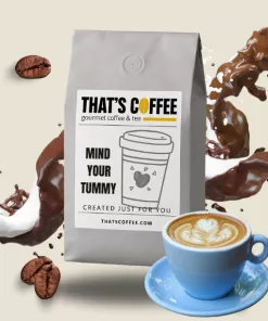 A bag of “That’s Coffee” gourmet coffee labeled “Mind Your Tummy,” surrounded by coffee beans, splashes, a cup of latte with foam art, and hints of premium coffee blends for a rich experience.