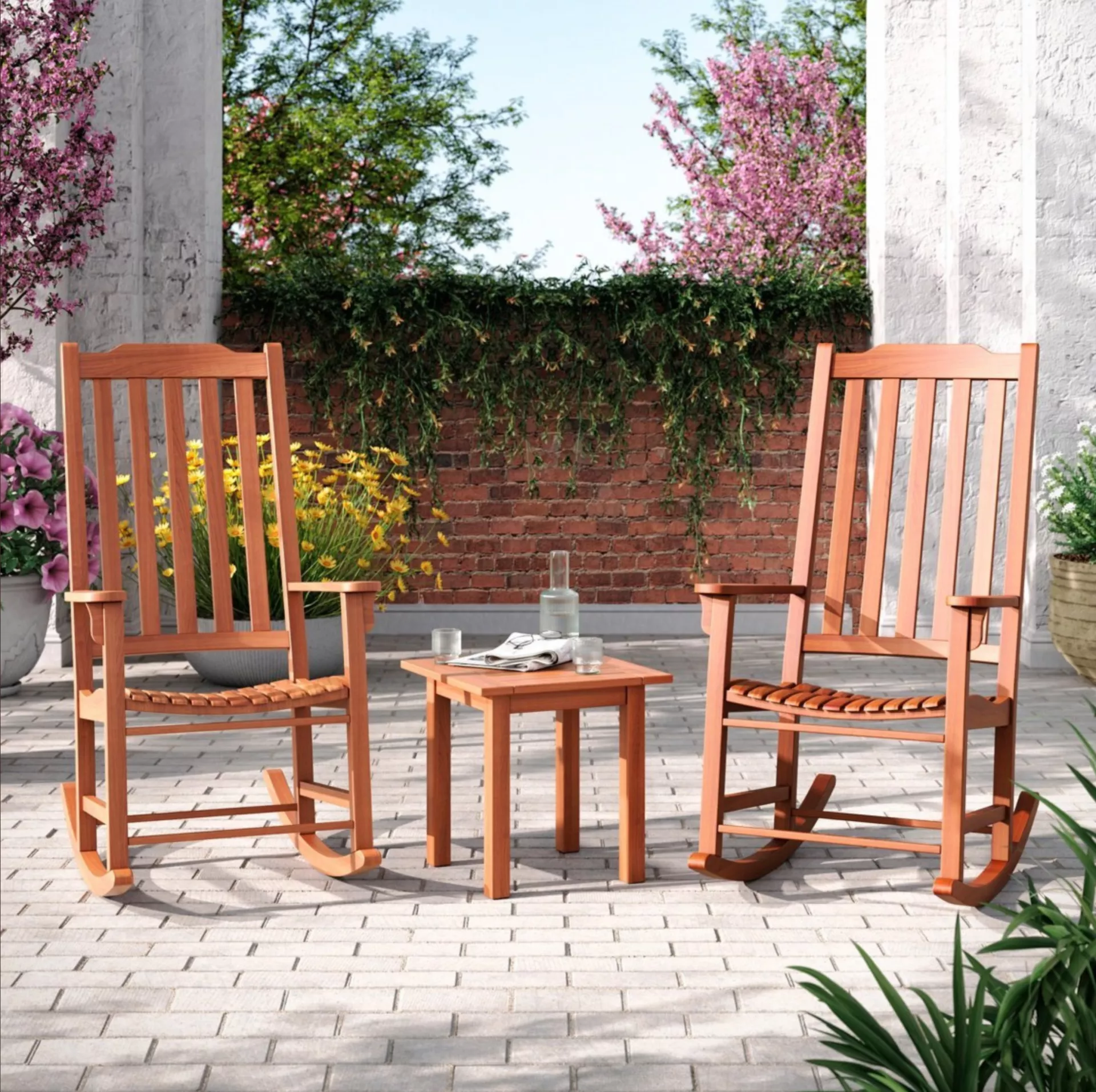two brown outdoor rocking chairs on a patio and a wooden coffee table with water and glasses on top of the table
