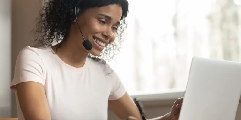Woman with headset taking notes during remote call at home office.