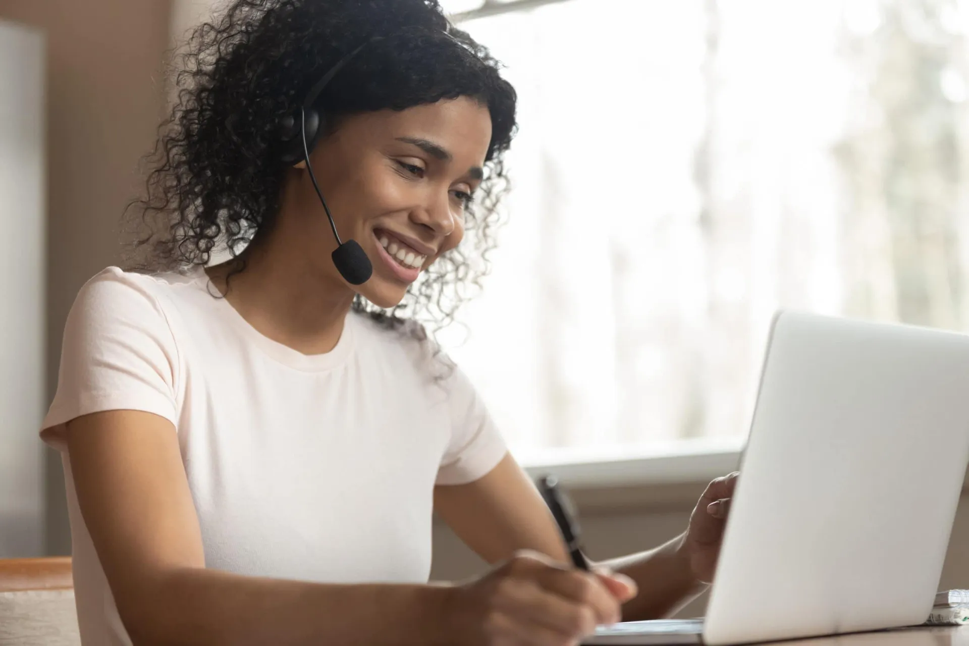 Effective remote calling tips for productivity and professionalism Woman with headset taking notes during remote call at home office.