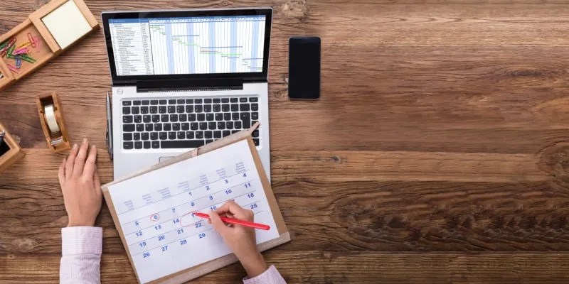 Business professional reviewing sales appointment schedule on laptop and calendar.