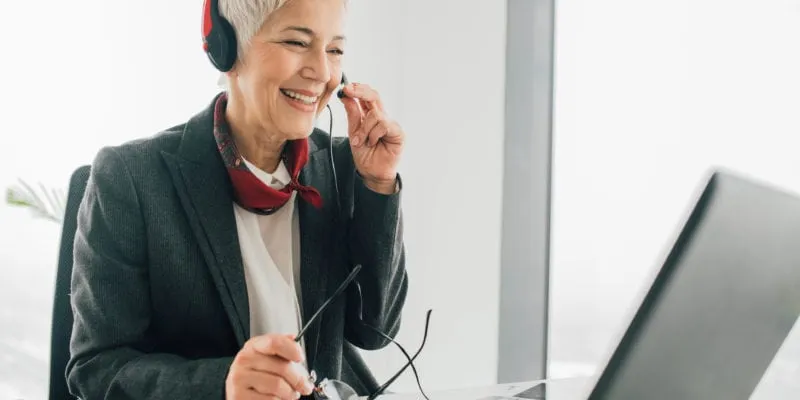 Smiling woman with headset making a cold call at her desk, improving sales techniques.