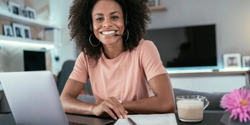 Smiling woman working at home with laptop and notepad, representing a business development professio.