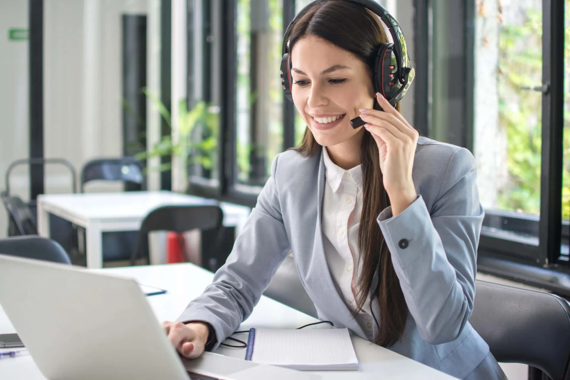 Customer support representative assisting clients remotely Customer support agent wearing a headset, working on a laptop in a modern office setting.