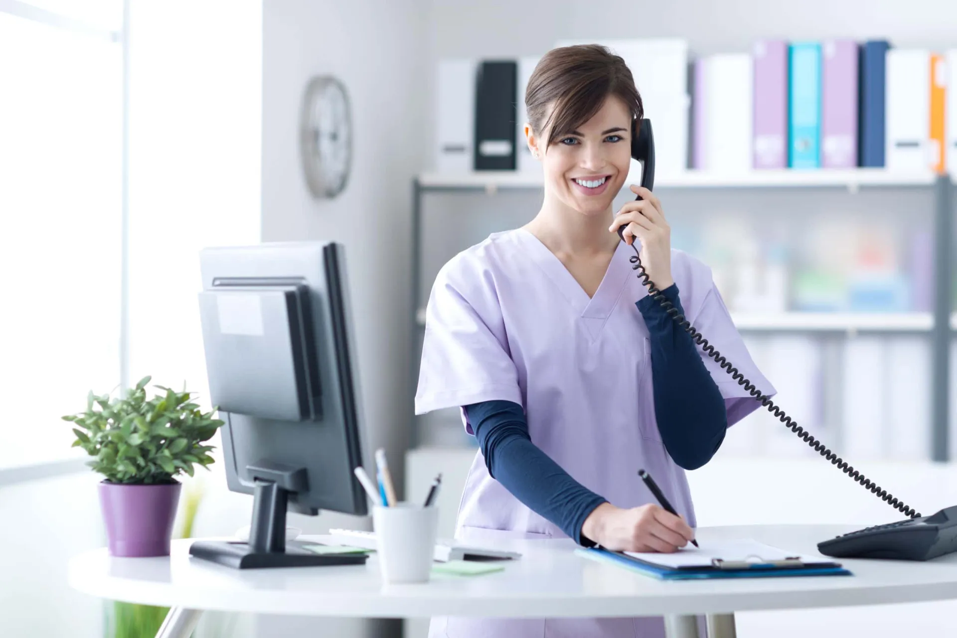 Customer Service Representative Using Phone Woman in healthcare uniform making a phone call at her desk.