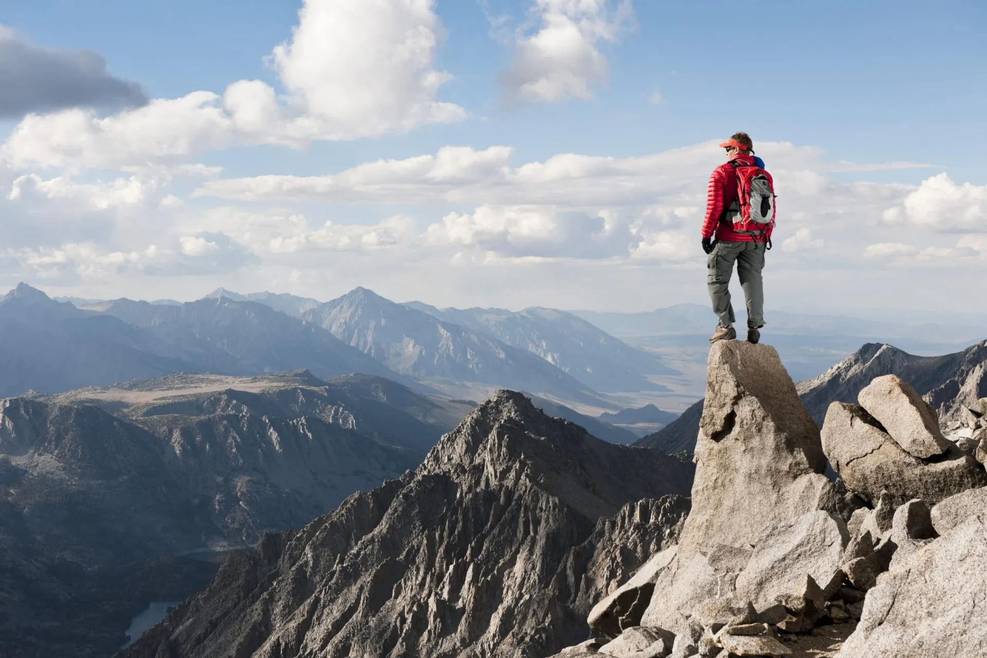 Climber on Mountain Peak Hiker standing on rocky mountain peak with scenic mountain range in background.