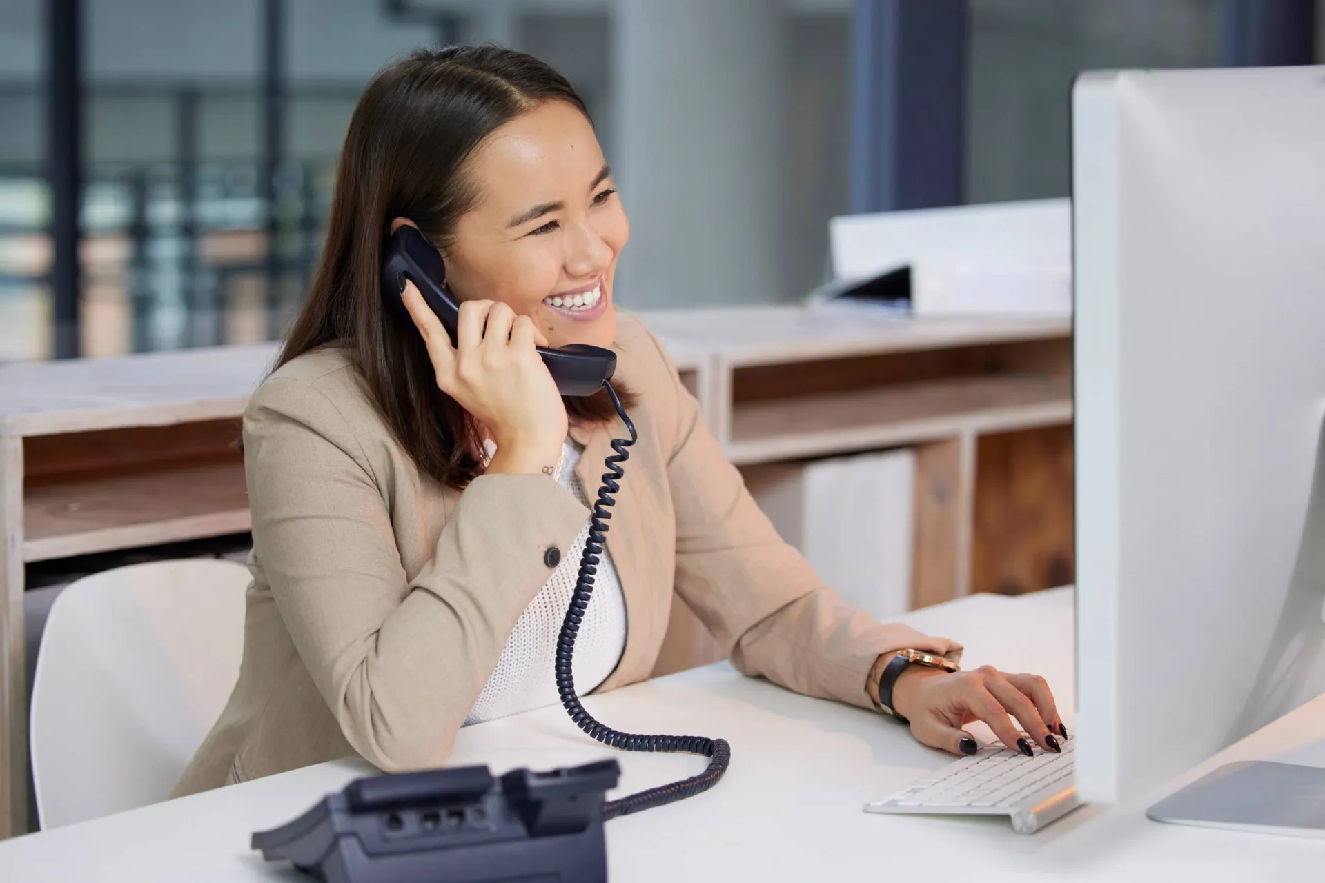 Sales prospecting with phone calls and CRM tools. Woman making sales calls at her desk with computer and phone.