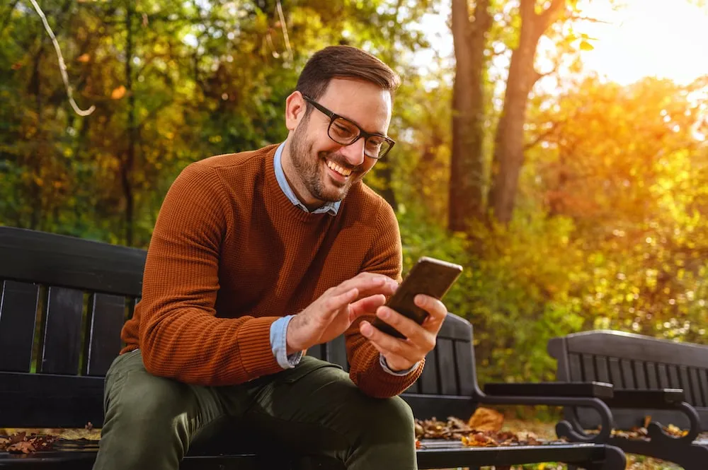 Warm Fall Sales Calling Campaign Smiling man using smartphone outdoors during autumn, boosting fall sales.