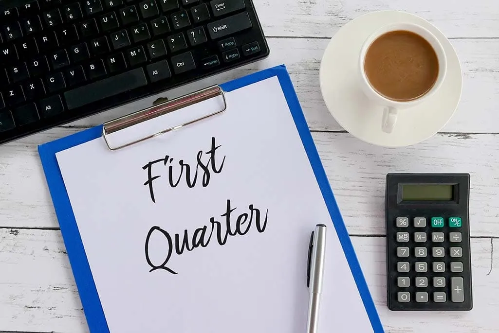 First Quarter Business Planning Computer keypad next to a note pad with First Quarter written on it next to a coffee and calculator focusing on Q1 success metrics.