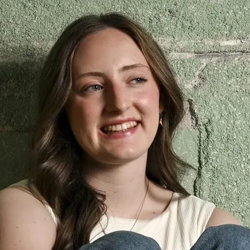 Pannell.Ellu_Silver A young woman sits in front of a textured wall, looking off-camera